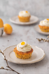 Lemon Poppy Seed Cupcakes with lemon curd and cream cheese topping and Fried Egg candies. Colourful Easter eggs, flowers on a stone background, top view. Easter holiday and festive food.