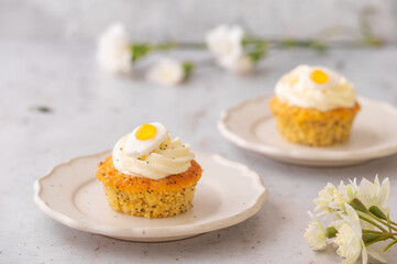 Lemon Poppy Seed Cupcakes with lemon curd and cream cheese topping and Fried Egg candies. Colourful Easter eggs, flowers on a stone background, top view. Easter holiday and festive food.