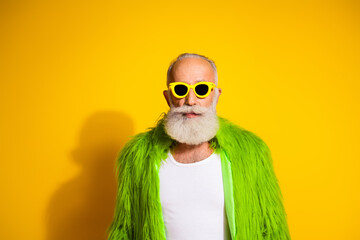 Eccentric elderly man in vibrant green outfit and sunglasses on yellow background portraying quirky style and confidence