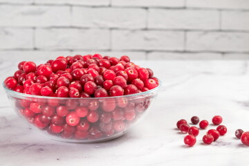 Frozen cranberries in transparent bowl, on light background. Preservation of vegetables and fruits. Natural products
