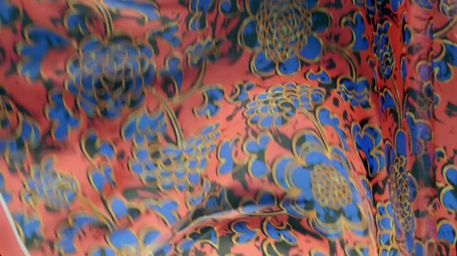 Red fabric with beautiful blue floral pattern falls, fluttering on a black background. Closeup. Macro. Slow mo, slow motion, high speed camera, 200fps