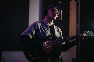 A musician passionately sings into a microphone while playing an electric guitar in a recording...