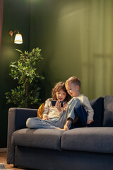 Obraz premium Brother and sister watching something on smartphone sitting on sofa at home