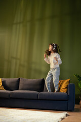 Naklejka premium Young girl jumping on sofa listening music with headphones