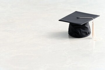single graduation cap gently rests alone on smooth light-colored surface its tassel perfectly positioned minimalist