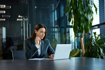 Determined professional in elegant suit concentrating on laptop in sleek corporate setting. Concept of ambition, digital transformation, entrepreneurship, decision-making.