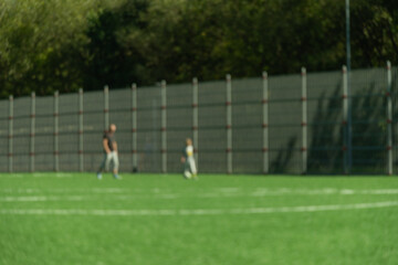 Obraz premium Green artificial turf football field with blurred athletes. Football players training on outdoor green artificial turf field. Abstract background. Mock up for montage product display or design your