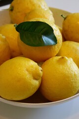 Close-up of fresh lemons in a bowl, with a single green leaf, capturing the vibrant color and freshness of citrus fruit.