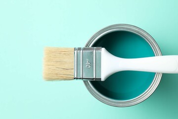 Can of bright paint and brush on turquoise background, top view