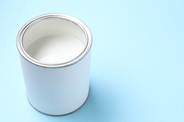 Can of white paint on light blue background, closeup. Space for text