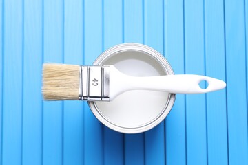 Can of white paint and brush on light blue wooden table, top view