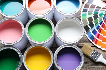 Cans of bright paints, brush and color palettes on wooden table, above view