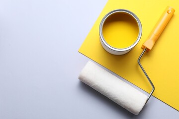 Can of yellow paint and roller on color background, flat lay. Space for text