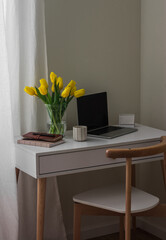 A bouquet of yellow tulips, a laptop, a notebook, a cup of coffee on a white table