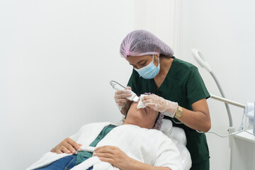 Beautician performing facial skin treatment on patient in clinic