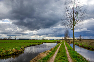 Cart track between ditches in a polder near Hoornaar, The Netherlands under a dramatic sky