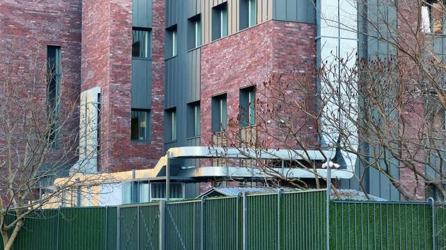 Modern Factory Building Exterior with Red Brick and Black Metal Siding Facade - Industrial Facility with Ventilation Ducts and Green Fence in Autumn - Establishing Shot 