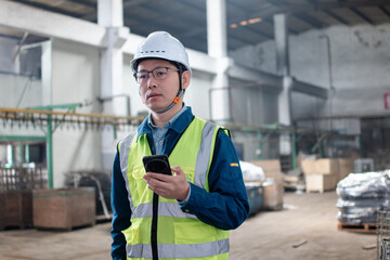 Asian male blue-collar workers are using mobile phones in the warehouse.