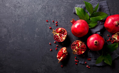 Fresh pomegranates with green leaves on the table. Dark grey background. Copy space. Top view. © annapustynnikova
