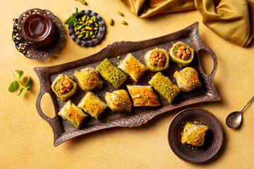 Turkish baklava on a cooper tray and a glass of tea. Yellow background. Close up. Top view.