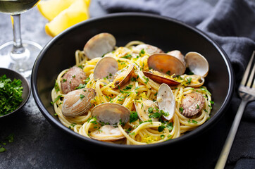 Spaghetti alle vongole, seafood pasta with clams in a black bowl and glass of wine. Dark background. Close up.