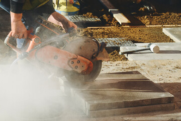 Construction worker operates concrete saw on building site while dust and debris fill the air