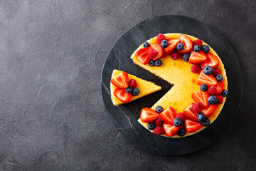 Cheesecake dessert with fresh berries on marble cutting board. Dark gray background. Copy space. Top view.