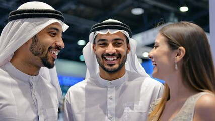 Smiling Arab businessmen interacting warmly with an international female attendee at a global conference event. Concept of multicultural business relations and networking.