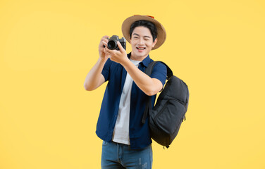 Obraz premium Portrait of young asian man wearing backpack and using camera posing on yellow background