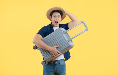 Portrait of a young Asian man holding a travel suitcase and posing against a yellow background