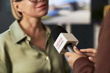 Close-up of journalist holding microphone and interviewing businesswoman in office