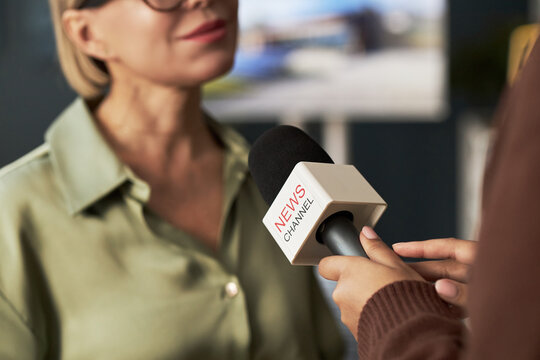 Close-up of journalist holding microphone and interviewing businesswoman in office