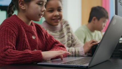 Little Asian girl working on laptop sitting at table with biracial girl and Asian boy, studying together in modern well-equipped classroom - Powered by Adobe