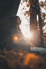 A young woman in a coat sits thoughtfully alone in an autumn forest against a background of fallen leaves. Autumn. Loneliness. Depression