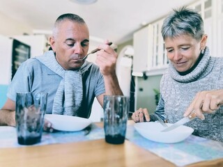 Happy couple eating at table with appetite.Woman and man in love eating,sitting at table in their comfortable home.Couple rests at home eating happily.Hungry adults at table