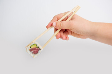 Close-up of a hand using chopsticks to hold a fresh sushi California roll with tuna, avocado, and sesame seeds against a clean white background. Minimalist and appetizing.