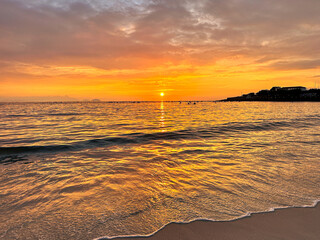 Beach sunrise with reflections in the water and white foam on the sand