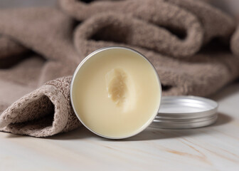 Opened body butter jar near light brown bath towel close up, herbal cosmetics for bodycare