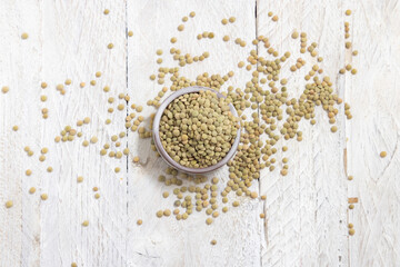 Bowl full of dried raw green lentils on white table top view. Traditional mediterranean legume