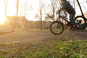 Child riding a bike in a park at sunset, jumping off a ramp with bare trees and golden sunlight in the background. Perfect for outdoor adventure and family fun photography.