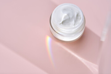 An open jar of cream with its texture on a pink background.
