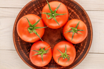 Several juicy red tomatoes with a clay plate on a wooden table, top view, close-up.