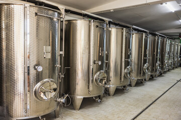 Stainless steel fermentation tanks lined up in a winery's production facility during the harvest season