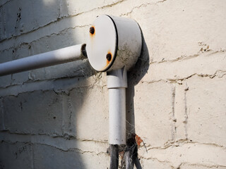 Plastic protective cover on electric power cable outside attached to brick wall.