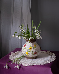Delicate fresh snowdrop flowers arranged beautifully in a charming ceramic pitcher on vibrant and colorful fabrics
