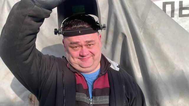 The worker takes off his welder's mask and smiles. The welder smiles after a hard day at work.
