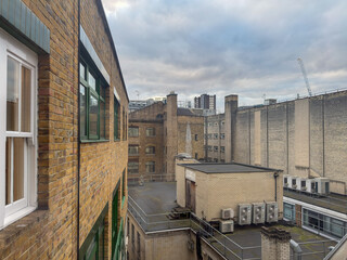 View across rooftops in an urban area featuring brick buildings, industrial air conditioning units, and a cloudy sky. 