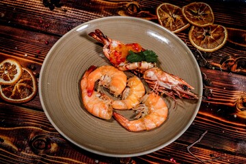 Aromatic Grilled Shrimp Drizzled with Zesty Sauce and Garnished with Fresh Greens, Served on Ceramic Plate with Dried Citrus Slices on Dark Wooden Background.