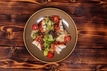 Gourmet Presentation of Salad with Grilled Eel, Fresh Salad Leaves and Cherry Tomatoes on Plate, Sprinkled with Sesame Seeds, Wooden Table, Top View.