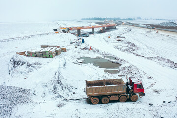 Construction of a bridge over the newly developed Highway D35, captured from above with a heavy duty truck on the snowy construction site during earthworks.